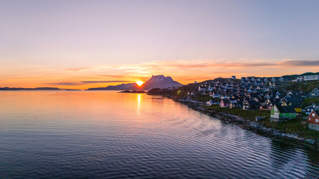 Aerial view of colorful houses on the rocky shoreline at sunset with a mountain peak in the distance in Nuuk, Sermersooq Municipality, Greenland.