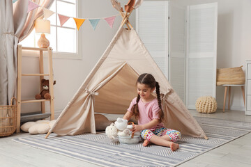 Little girl playing with toys near toy wigwam in playroom © New Africa