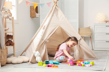 Little girl playing with building blocks near toy wigwam in playroom © New Africa