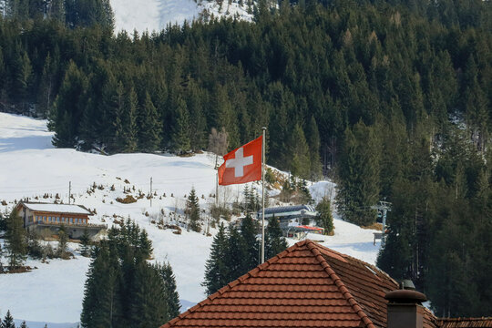 Swiss flag waving proudly in the mountains with snowy peaks and blue skies in the background