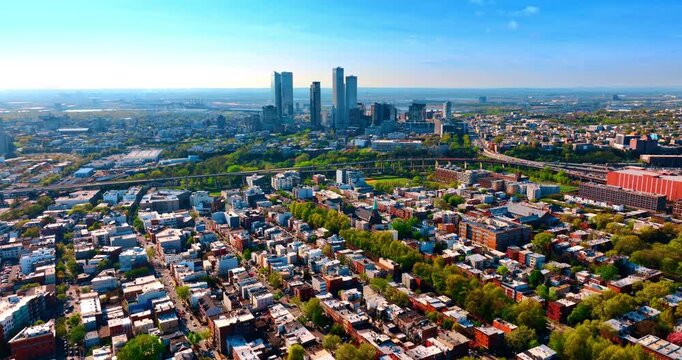 Flight over the low-rise urban landscape with lush greenery. Approaching the group of skyscrapers in the scenery. Jersey City, New Jersey, USA.