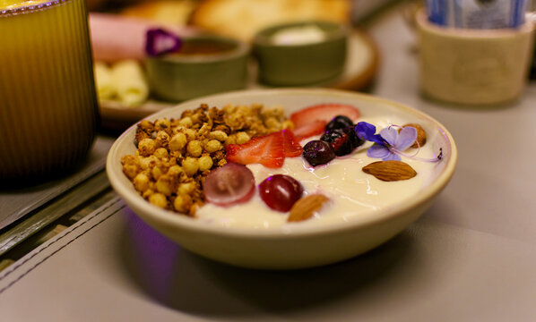 Desayuno saludable con yogur griego, granola crujiente, uvas frescas, fresas y almendras, decorado con flores. Primer plano desde un &aacute;ngulo elevado de una comida nutritiva. Fotograf&iacute;a con bokeh.