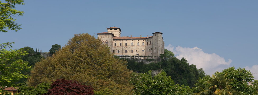 Angera, Italy - April 20, 2026: Rocca di Angera, historic medieval fortress overlooking Lake Maggiore in Lombardy, Italy, surrounded by lush green trees under clear blue sky.