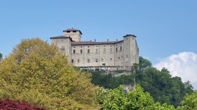 Angera, Italy - April 20, 2026: Rocca di Angera, historic medieval fortress overlooking Lake Maggiore in Lombardy, Italy, surrounded by lush green trees under clear blue sky.