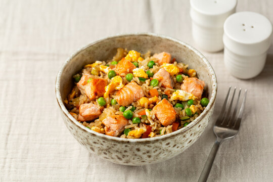 Salmon Fried Rice with eggs and vegetables, green peas, carrot, onion. Served in a bowl with a fork. Asian style food.