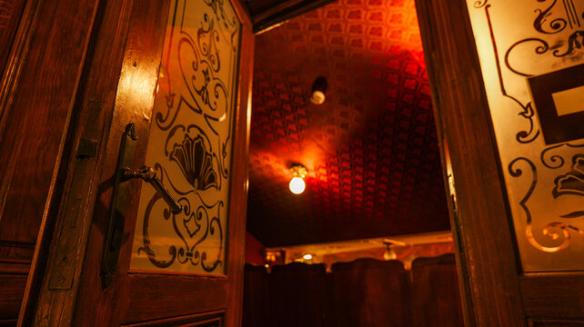 Vintage wooden door with ornate glass opens to a dimly lit, red-patterned room