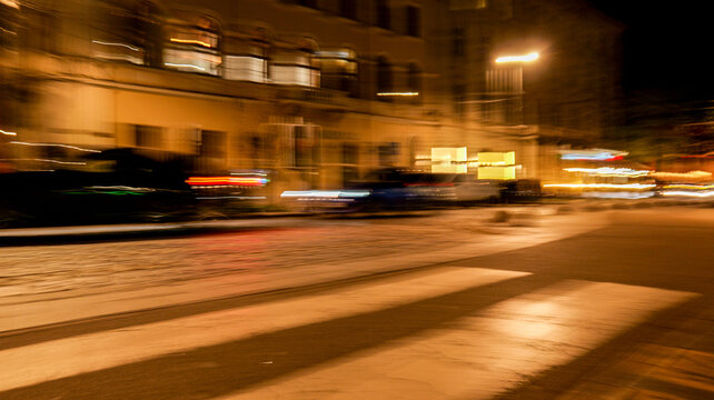 Blurry night street scene with light trails from moving vehicles and illuminated buildings