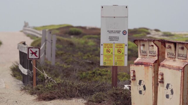 A walkway with a sign warning people of the hazards of water at Border Field State Park due to Tijuana River pollution