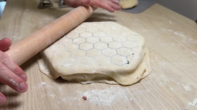 Hands roll dough on a floured wooden board with a honeycomb pattern pressed into the surface, warm kitchen scene suggesting homemade baking and careful preparation