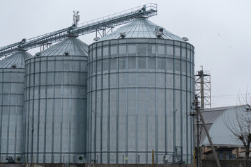 Obraz premium Grain Silos Stand in a Rural Area Under Cloudy Skies With a Rail Platform and Storage Buildings Nearby in Winter