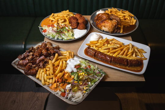 A mixed restaurant plate with crispy fries, falafel, sausages, fresh salad, and creamy sauces served on a wooden table.