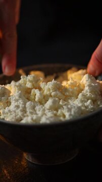 Close-up of female hands mixing fresh cottage cheese in a bowl with a spoon. Rustic homemade dairy preparation in a cozy kitchen with organic ingredients