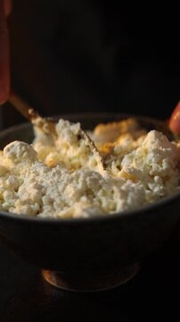Close-up of female hands mixing fresh cottage cheese in a bowl with a spoon. Rustic homemade dairy preparation in a cozy kitchen with organic ingredients