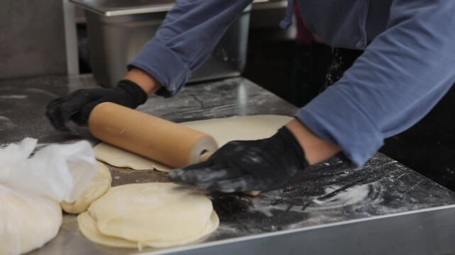 A female chef prepares traditional fried pastries in a professional restaurant kitchen, shaping dough and cooking fresh food by hand.