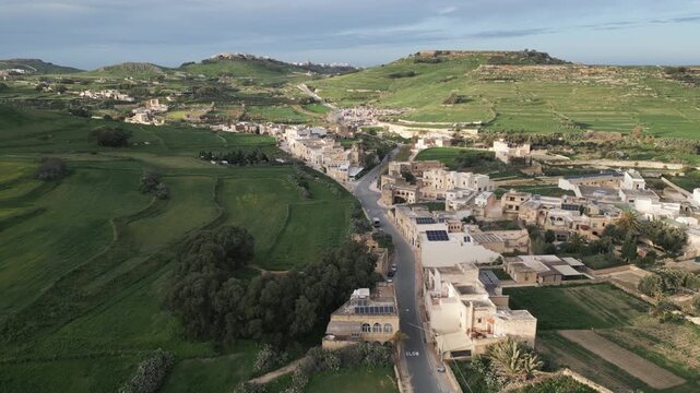 Forward drone flight over green rural landscape and stone houses on Gozo island, Malta. Late afternoon.