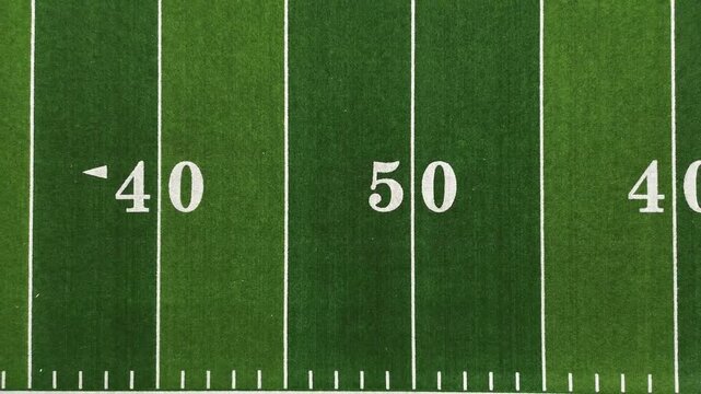 Aerial pull-away shot of an American football field showing the 50 yard line, hash marks and sideline