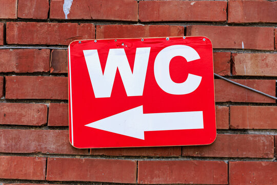 Red wc sign with arrow on brick wall indicating restroom direction