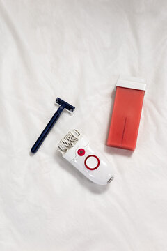 Red wax cartridge with wooden spatulas vs epilator vs razor. Compact devices arranged for DIY home wax depilation prep. Clean minimal styling. concept of choosing between hair removal products