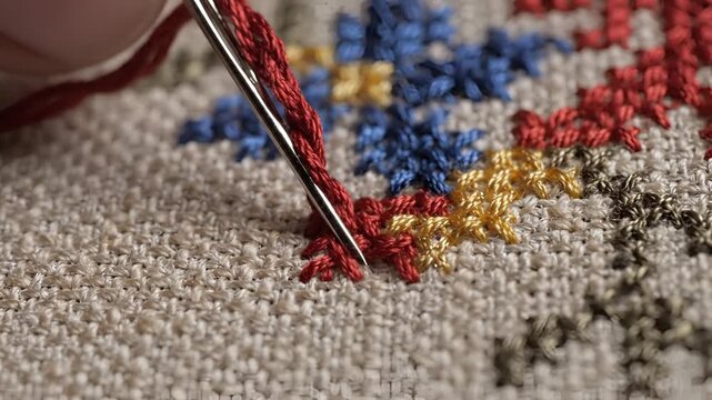 Closeup of needle and red thread creating crossstitch pattern on fabric.