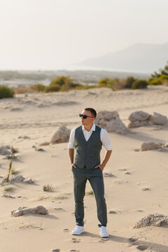 Stylish man in vest and sunglasses standing in sunny desert landscape