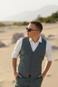 Stylish man wearing suit vest and sunglasses in desert