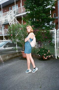 Young Woman with Backpack Standing Near Flowering Garden in Urban Cour