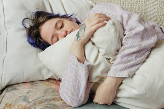 Tattooed person looking introspective lying down in the couch