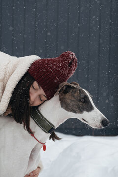 Woman hugs greyhound dog in snow during winter day