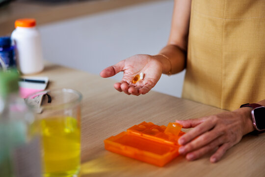 Person getting the day's pills from the pill organizer on the table