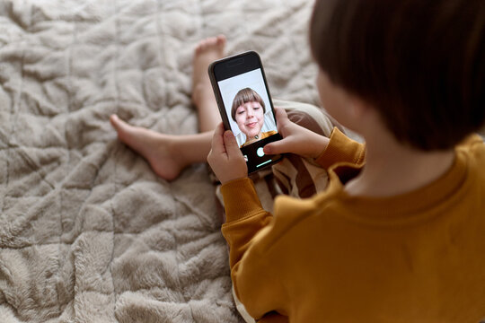 Child taking selfie with smartphone on bed