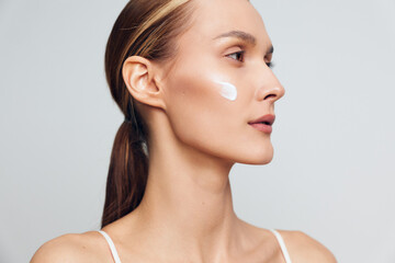 Obraz premium Woman applying face cream, skincare self care close up profile on a light gray background, soft studio lighting, smooth skin care concept, calm mood beauty routine