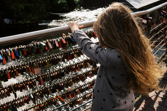 little girl holding onto railing that is covered in locks.