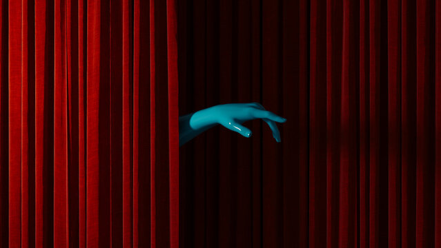 Hand reaches out from behind red curtain in theater setting