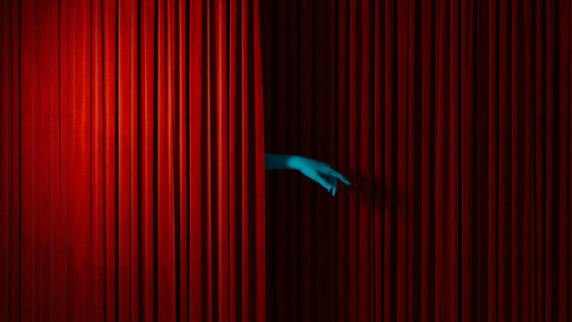 Hand reaches out from behind red curtain in theater setting