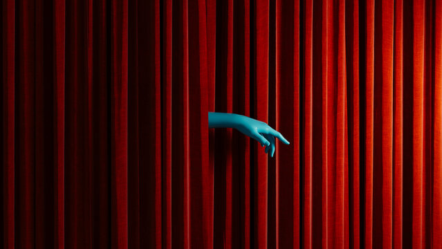 Hand reaches out from behind red curtain in theater setting