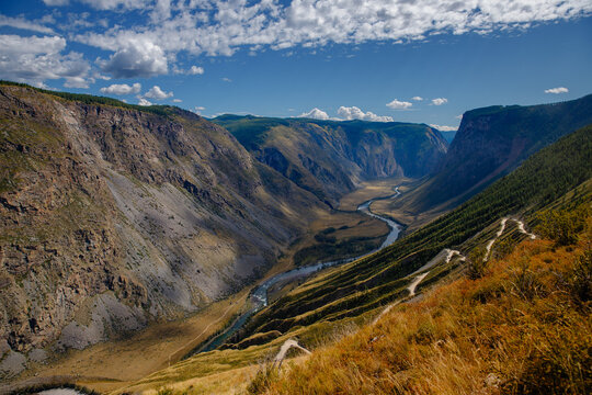 Majestic mountain valley with river and rugged cliffs under blue sky and fluffy clouds Katu Yaryk pass Altay