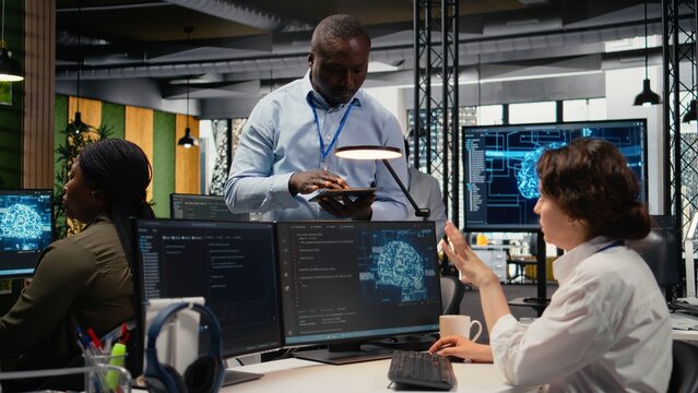 Manager talking with intern in office, using specialized hardware to accelerate complex AI calculations. Team leader teaching trainee how to manage machine learning training datasets, camera A