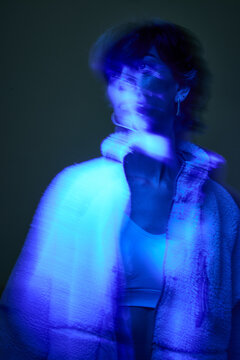 Young person poses in blue light wearing a stylish jacket indoor