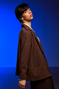 Person in brown jacket poses against blue background