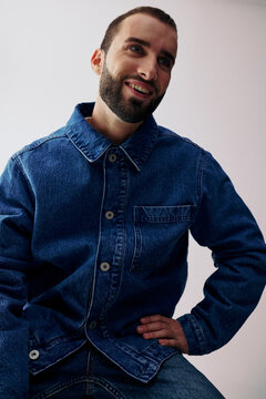 Man Poses in Denim Jacket Indoors With Neutral Background