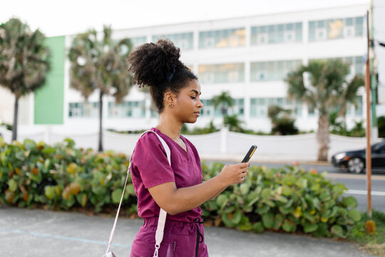 Young Woman in Medical Uniform Walking on a Street Using Phone