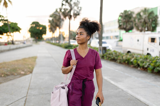 Young Woman in Medical Scrubs Walking on a City Street at Sunset 