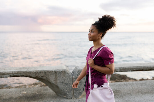 Young Smiling Hispanic Woman in Medical Uniform Walks Near the Ocean