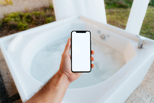 Hand Holds a Phone With White Screen Above a Hot Tub