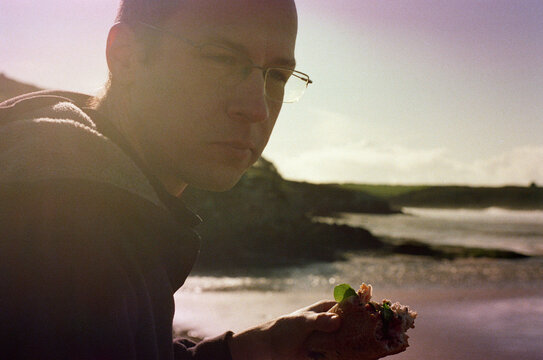 Candid portrait of a man eating a sandwich in front of the ocean.