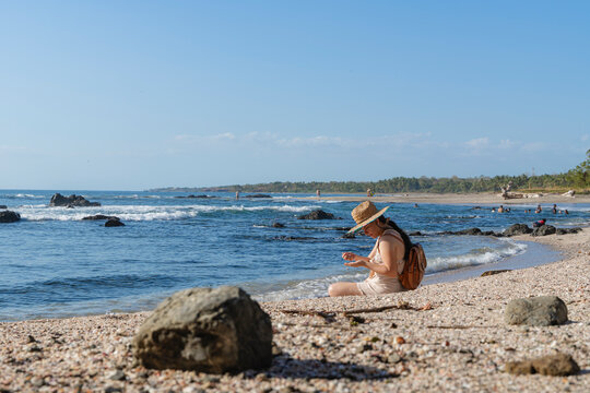 Woman sitting on the beach shore looking at sea shells.