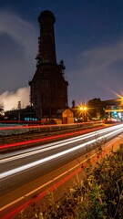 Fototapeta premium Long Exposure Night Photography of Industrial Chimney and Light Trails.