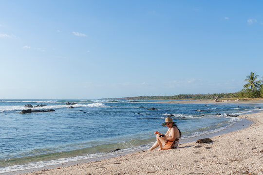 Smiling woman sitting on the beach sand looking at camera.