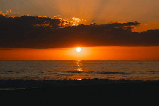 Setting sun on the sea horizon beneath a mantle of clouds.