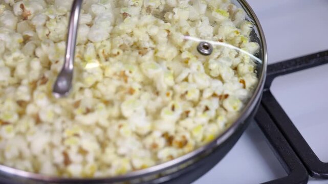Popcorn kernels popping in a hot pan. Delicious popcorn popping in a hot pan with a glass lid on a gas stove, creating a classic homemade snack for movie night with an explosion of fluffy